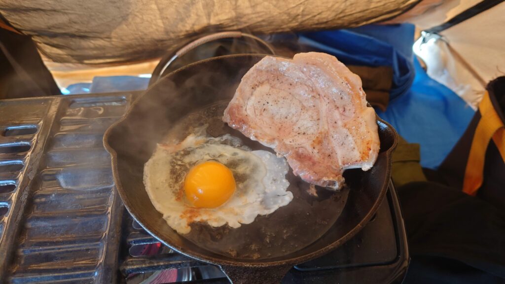 石油ストーブの上のスキレット、肉と卵の調理