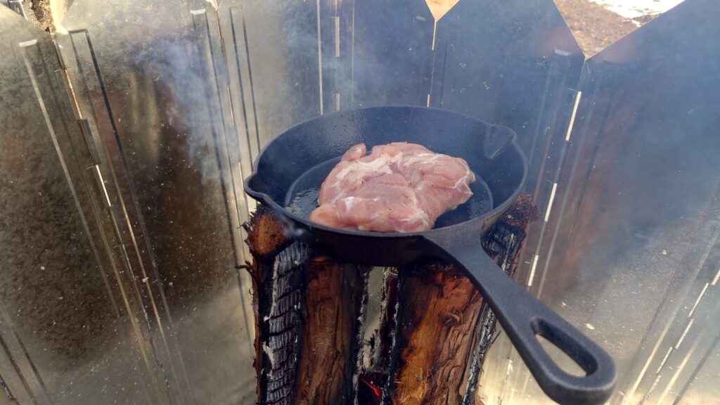 スウェーデントーチの上のスキレットで鶏モモ肉の調理