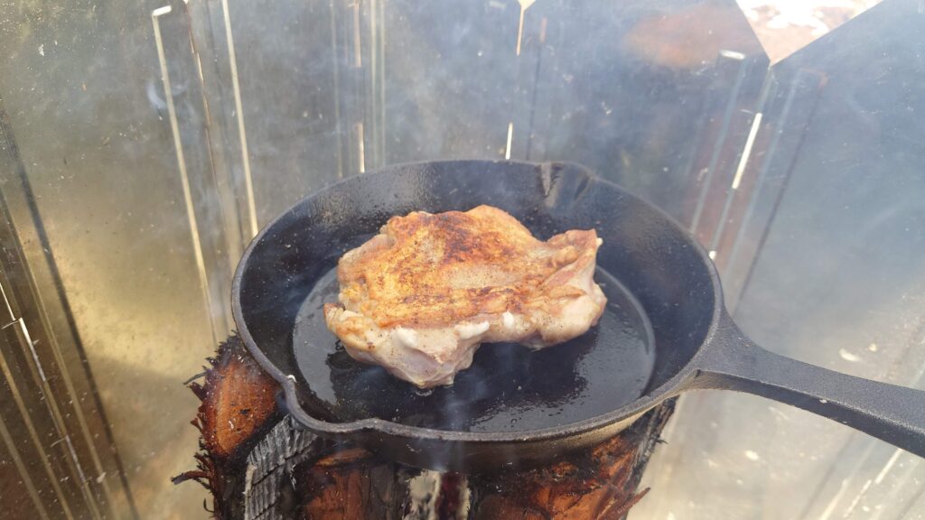 スウェーデントーチの上のスキレットで鶏モモ肉の調理、焼き色の付いた鶏皮