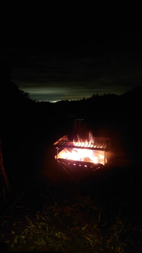 星空キャンプ場焚火と遠くの夜景